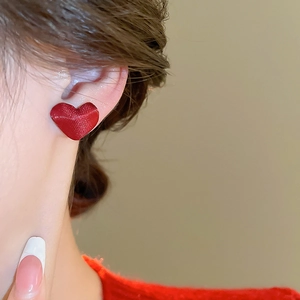 Primo piano di orecchini a cuore rosso satinato indossati da una modella in luce soffusa