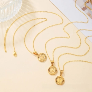 Detailed macro view of three golden initial disc necklaces featuring letters X, Z, and Y