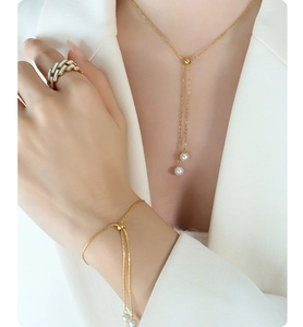 Close-up of elegant gold Y-necklace and bracelet set with pearls and white enamel ring