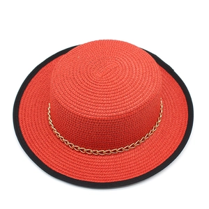 Détail d'un chapeau de paille rouge avec bordure noire et chaîne décorative en métal doré