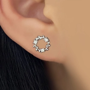 Detailed view of silver branch wreath earring with zircons worn on a female ear
