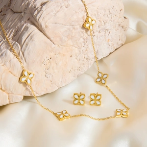 Detailed macro view of 18k gold clover necklace and matching earrings on white silk fabric
