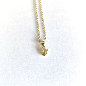Macro detail of polished gold letter U pendant necklace with a delicate chain