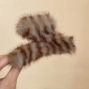 Gros plan d'une pince à cheveux en peluche à rayures marron tenue devant fond beige