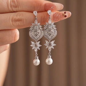 Detailed macro view of silver earrings with leaf, heart, cubic zirconia, and white pearls