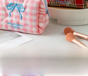 Detail of pink gingham cosmetic bag with blue bow embroidery and Sweet Store Supply logo