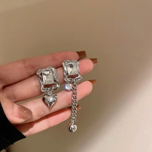 Macro detail of asymmetric silver earrings with square crystals and heart chain drops
