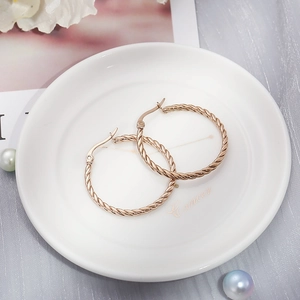 Detailed view of rose gold twisted rope hoop earrings resting on a white display tray