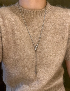 Detail of silver Y-shaped drop pendant necklace on brown sweater background