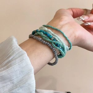 Close-up of Bohemian layered bead bracelets in grey, blue, green, and white on wrist