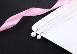 Elegant white pearl necklace with silver chain on a black background and pink ribbon