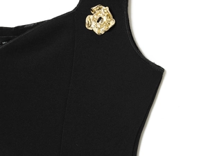 Detail of black knit top featuring a delicate golden flower metal ornament on the fabric