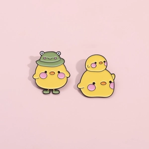 Detailed view of cute yellow chick enamel pins with green frog hat and tiered design