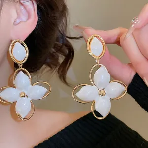 Élégantes boucles d'oreilles pendantes fleurs dorées et blanches portées par un mannequin