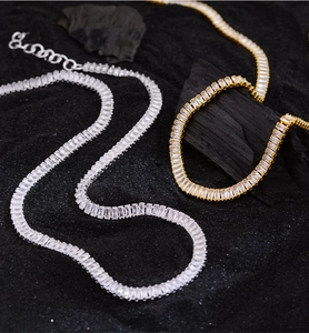 Detailed close-up of gold and silver tennis necklaces with baguette-cut zircons on black sand