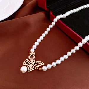Vue macro du pendentif papillon doré et perles blanches sur soie marron