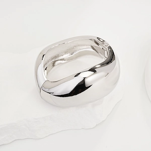 Macro shot of wide silver polished metal cuff bracelet on stone stand with glossy finish