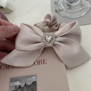 Detail of elegant champagne satin bow hair tie with sparkling heart rhinestone centerpiece