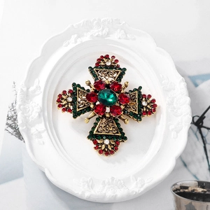 Detail of a vintage golden cross brooch with red and green crystals on a white plate