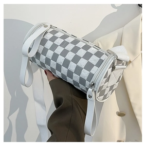 Detailed macro view of checkerboard textured cylinder shoulder bag with wide strap
