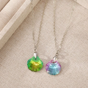 Close-up of shell-shaped gradient crystal pendants in green and purple on linen
