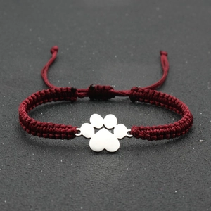 Close-up of handmade red woven lucky bracelet featuring a silver dog paw charm
