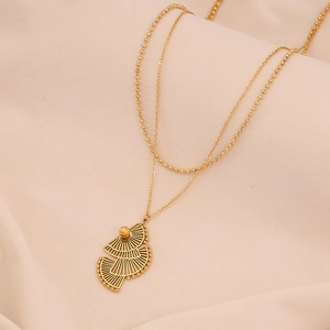 Détail d'un collier doré à double rangée avec pendentifs en éventail sur tissu beige