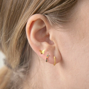 Detailed view of gold butterfly stud and colorful zircon earrings on a female ear