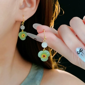 Close-up of gold plated flower earrings with green jade petals and red zircon detail