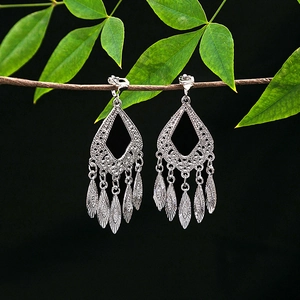 Detailed macro view of silver ethnic tassel clip earrings on a natural branch