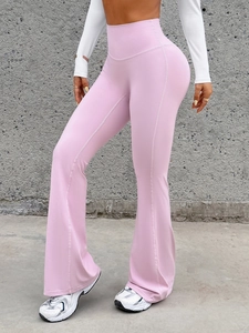 Pink high-waisted flare yoga pants shown on model against a concrete wall background