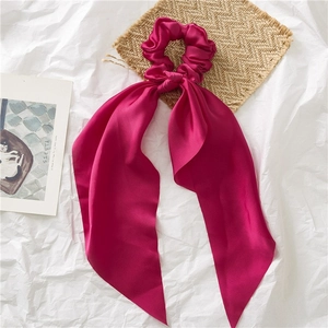 Detail of rose red satin scrunchie with long ribbon on a white textured background