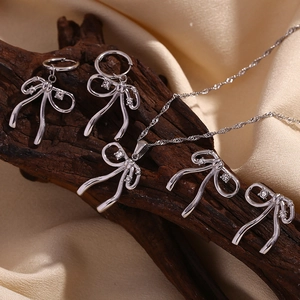 Macro detail of silver bow pendant necklace and matching earrings with white crystals