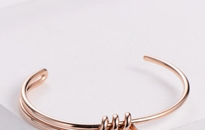 Detail shot of rose gold knotted open bangle showing triple spiral wrap on stone surface
