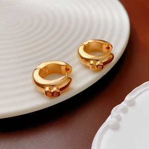Macro shot of gold hoop earrings featuring a circular B-shaped charm on white tray