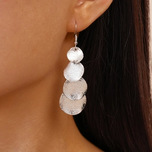 Gros plan de boucles d'oreilles argentées mates géométriques irrégulières à texture martelée