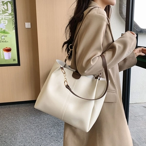 Chic off-white tote bag with brown straps and gold chain detail shown on a model