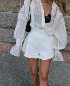 Detail of white puff sleeve sheer shirt and high waist shorts set in outdoor natural light