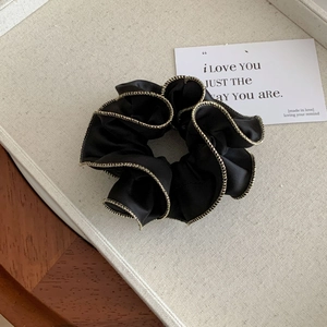Détail d'un chouchou en satin noir avec bordure dorée ondulée sur plateau beige