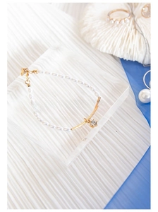 Nahaufnahme von Perlenarmband mit goldener Röhre und Kristallanhänger auf Acrylständer