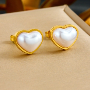 Macro de boucles d'oreilles cœur dorées avec perle blanche sur surface beige
