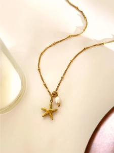 Detail of a gold starfish pendant with a small white pearl on a delicate beaded chain