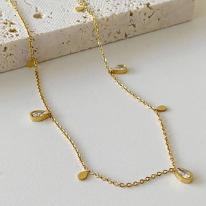 Elegant gold fringe necklace featuring teardrop cubic zirconia and round metal pendants