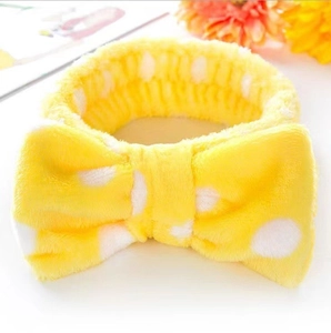 Close-up of yellow plush headband with white polka dots and oversized decorative bow