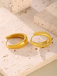 Close-up of chunky gold-plated stainless steel oval hoop earrings on beige stone base