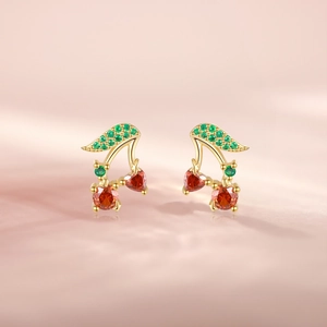 Macro shot of cherry-shaped earrings with red and green gemstones on pink background