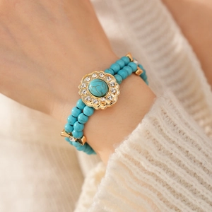 Gros plan d'un bracelet en perles turquoise avec pendentif fleur dorée au poignet