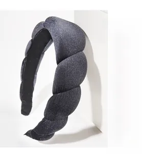 Detail of a thick black braided headband in shimmering fabric with non-slip inner grip