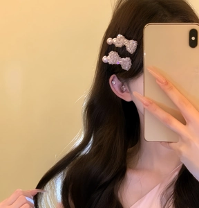 Close-up view of elegant pink pearl bow hair clips worn on wavy hair in a mirror selfie