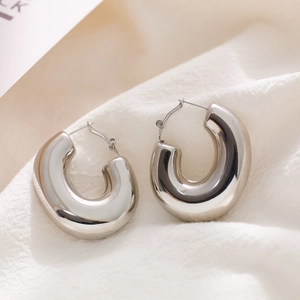 Detailed macro view of polished thick C-shaped silver hoop earrings on white fabric